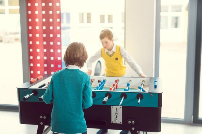 Twee kinderen spelen samen tafelvoetbal, ook wel bekend als kickertafel.